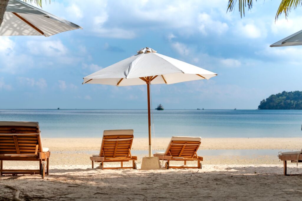 Amazing scenery of tropical sandy beach with cozy wooden sunbeds under umbrellas against picturesque blue sea on clear sunny day